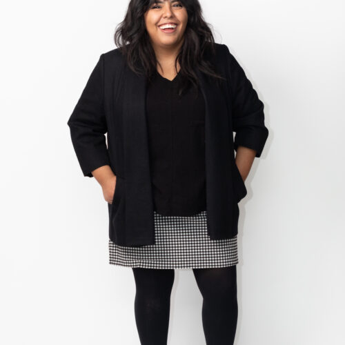 Ruby in a block shirt and jacket with a black and white skirt, smiling.